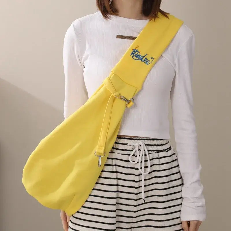 Stylish yellow cat carrier sling bag worn crossbody for traveling with small pets outdoors.