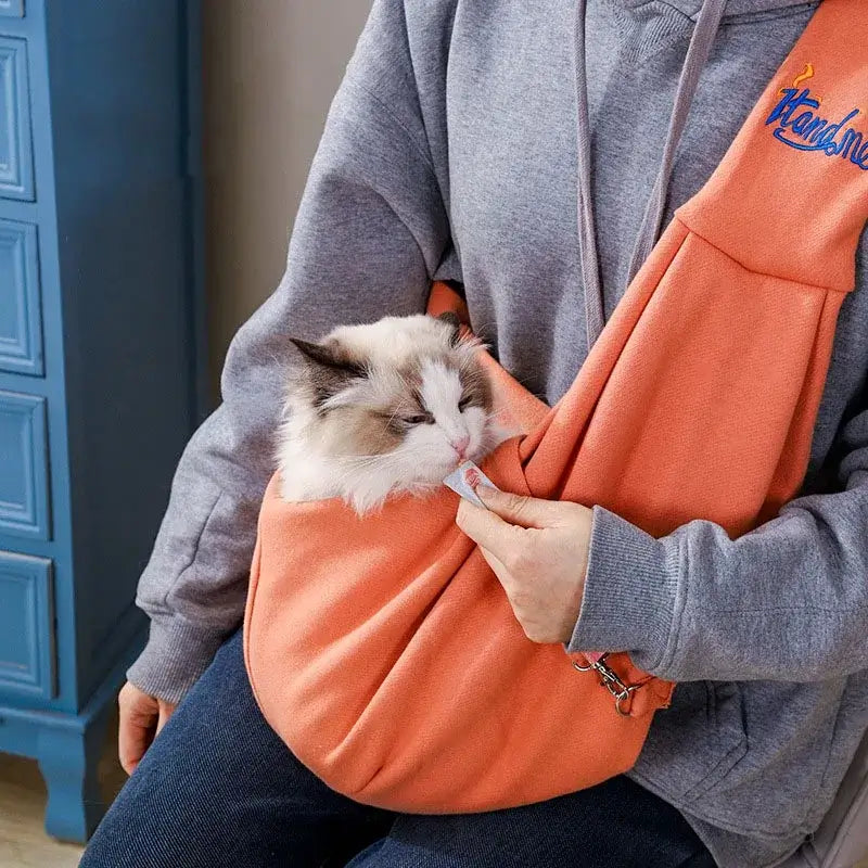 Orange crossbody cat carrier bag with a cat inside, designed for outdoor travel with pets.