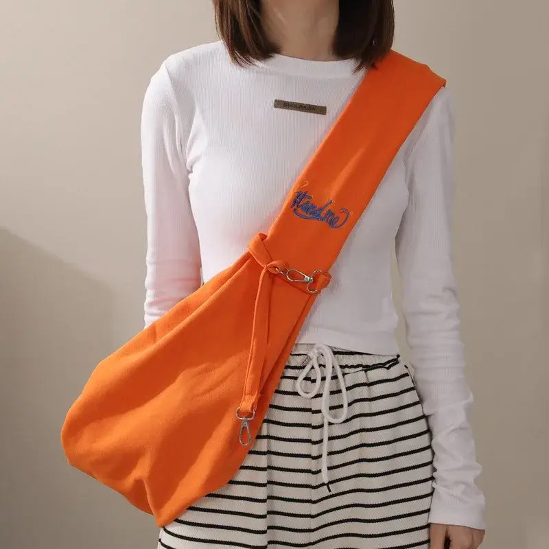 Orange crossbody cat carrier bag worn by a person, suitable for outdoor travel with pets.